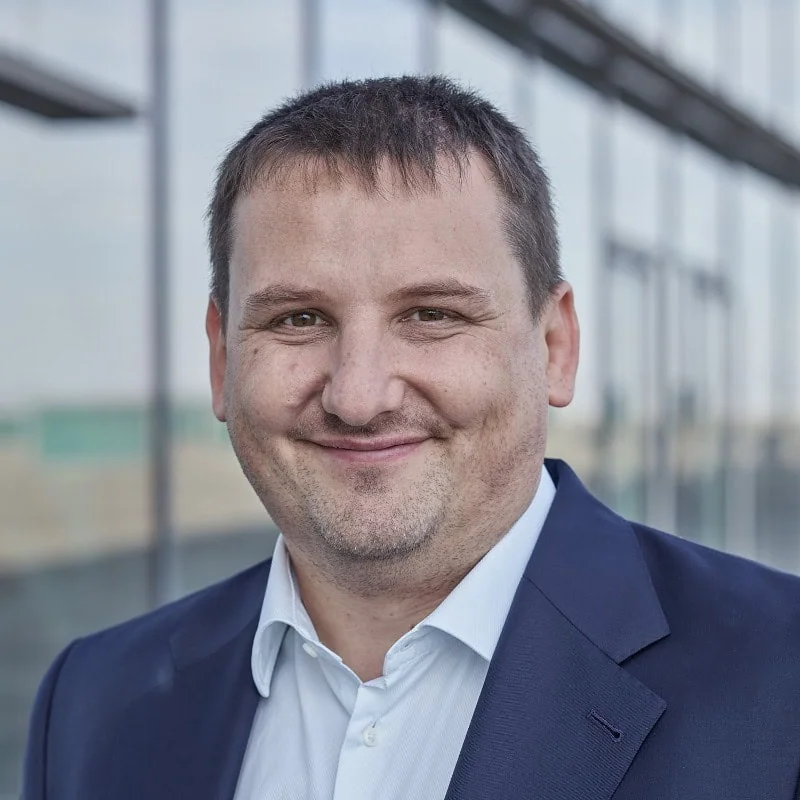 Ralf Schäfer, professionell im Business-Kontext, lächelt in einem modernen Gebäude.