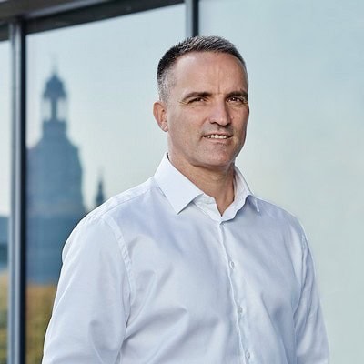 Frank Kaiser in Businesskleidung vor einem Fenster mit Stadtblick.
